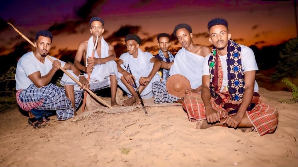 Young Somali men in traditional clothing sitting together on sand at sunset