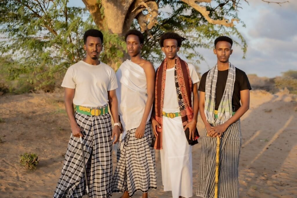 Four young Somali men in traditional macawiis and shawls standing under a tree