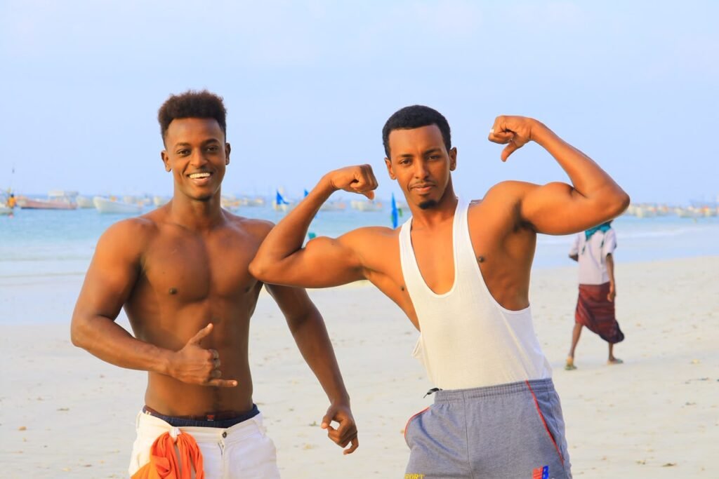 Two young men flexing their arms and smiling on a beach