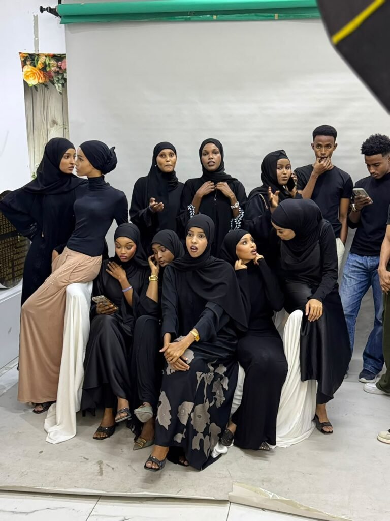 Group of young Somali women in black abayas posing together, with young men standing behind them